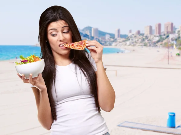 Portrait of young woman eating pizza and looking salad against a Stock Photo