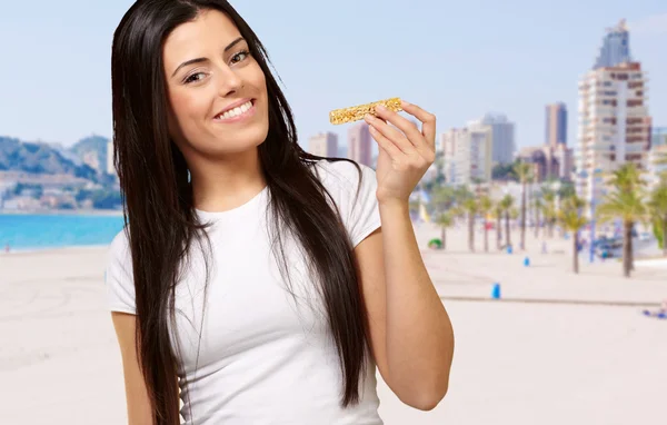 Portrait of young woman eating cereal bar against a beach Stock Picture