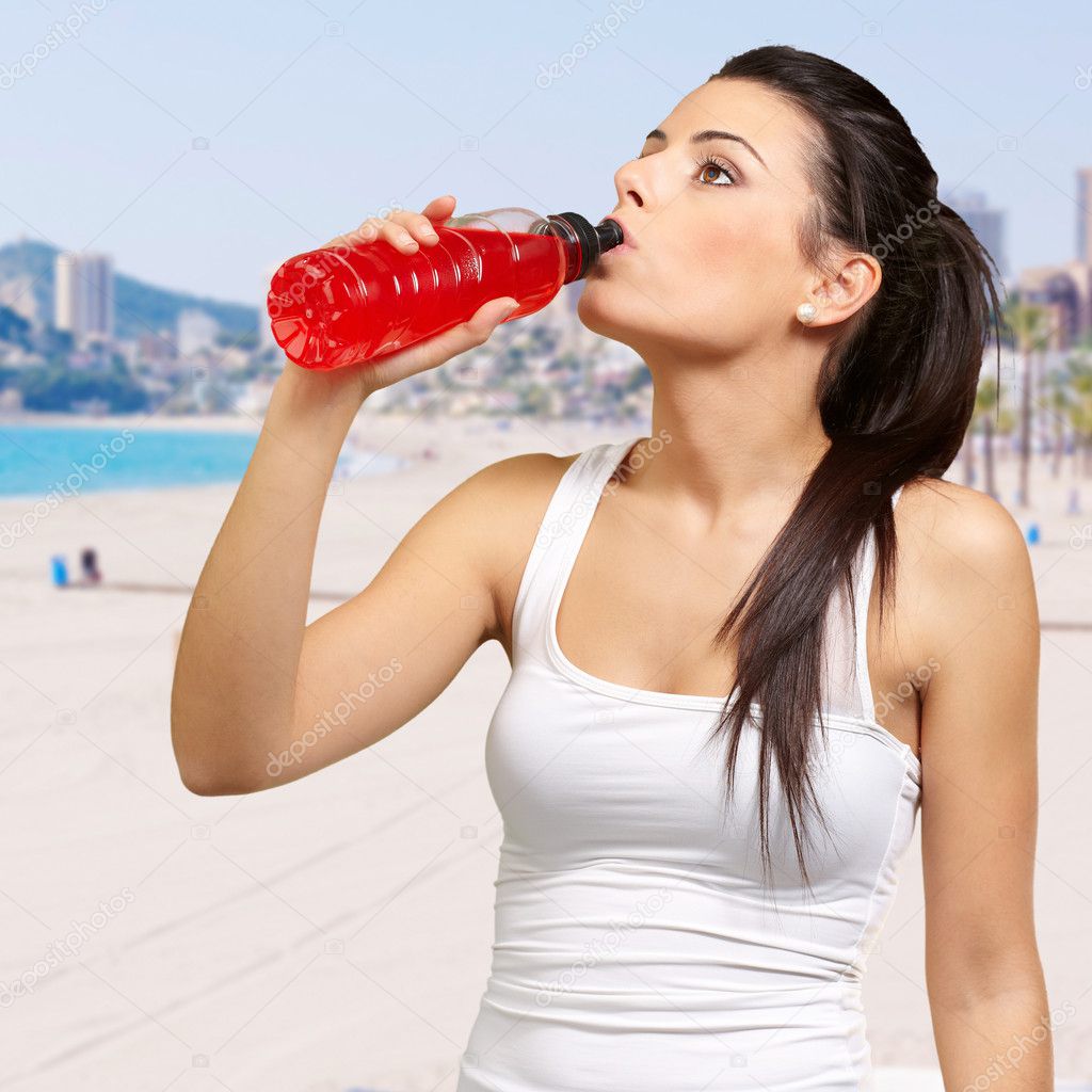 Portrait of young sporty woman drinking isotonic drink against a