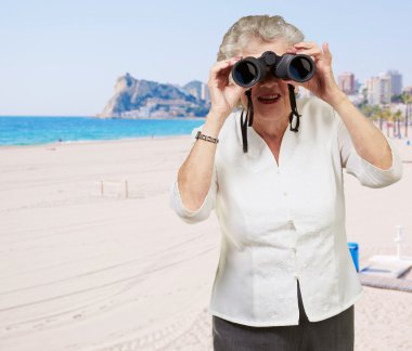 Portrait of senior woman looking through a binoculars in the bea clipart
