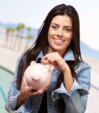 Portrait of young woman saving with piggy bank near the beach clipart