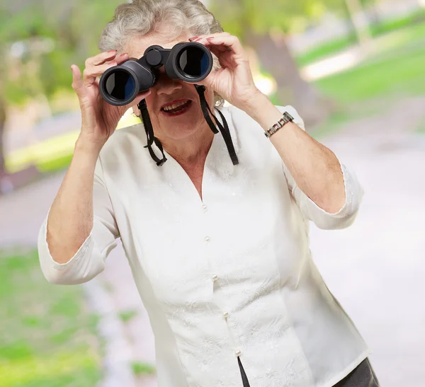 Retrato de mulher sênior olhando através de um binóculos no parque — Fotografia de Stock
