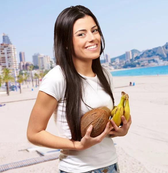 Ritratto di giovane donna che tiene frutta tropicale vicino alla spiaggia — Foto Stock