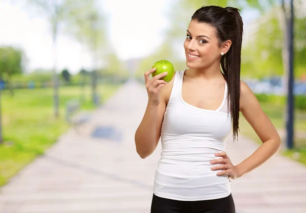 Retrato de una hermosa joven sosteniendo una manzana verde en el parque —  Fotos de Stock