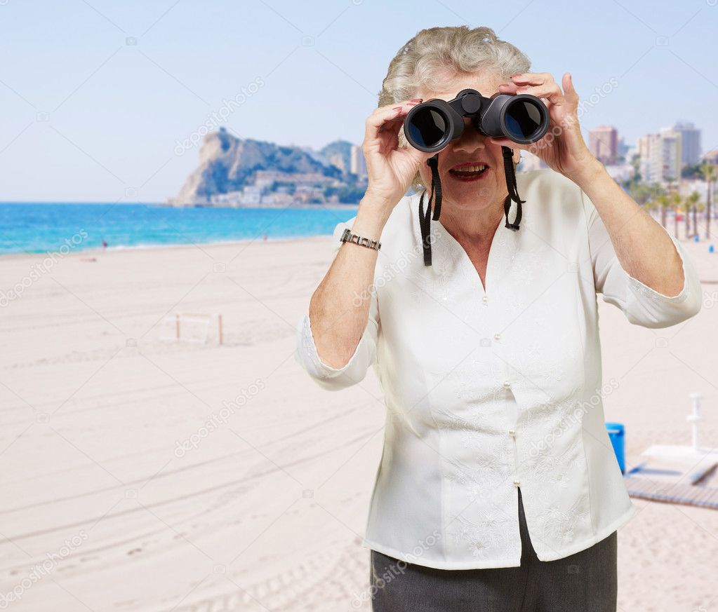 Portrait of senior woman looking through a binoculars in the bea