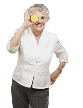 Portrait of senior woman with lemon in front of her eye over whi