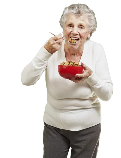 Femme âgée mangeant des céréales dans un bol rouge contre une ba blanche — Photo