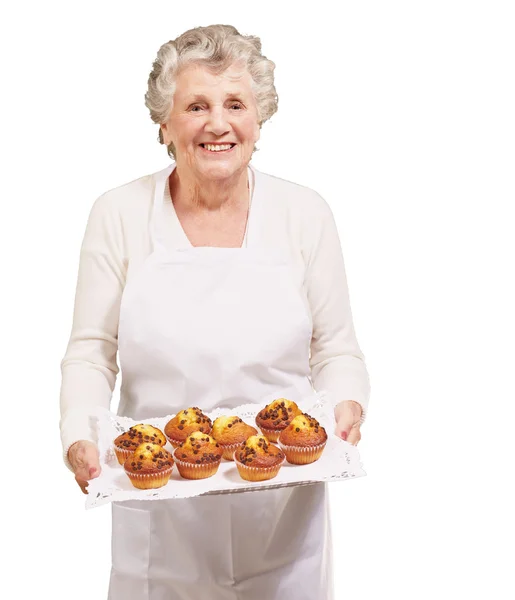 Portrait of cook senior woman holding a chocolate muffins tray o — Stock Photo, Image