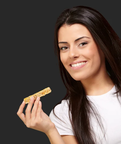 Muotokuva nuori nainen syö murobaari mustalla taustalla — kuvapankkivalokuva