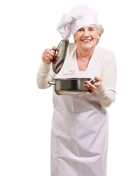 Portrait of cook senior woman opening sauce pan over white — Stock Photo, Image