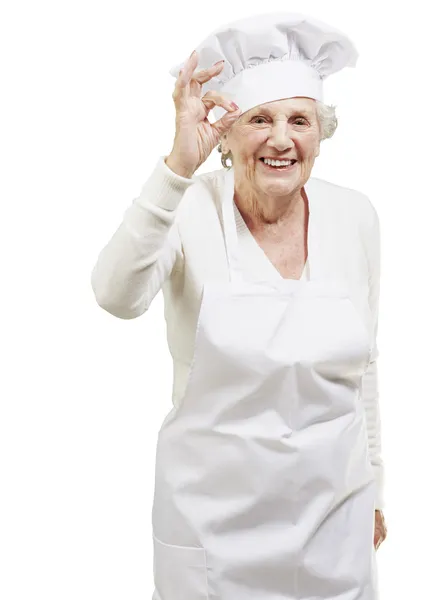 Äldre kvinna kock gör en utmärkt symbol mot en vit baksida — Stockfoto
