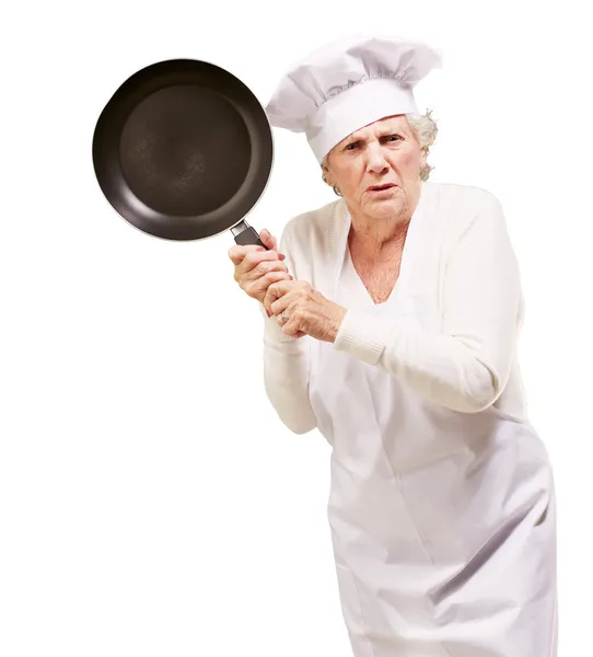 Кухарка старша жінка сердиться, намагаючись вдарити з каструлею на білому фоні — стокове фото