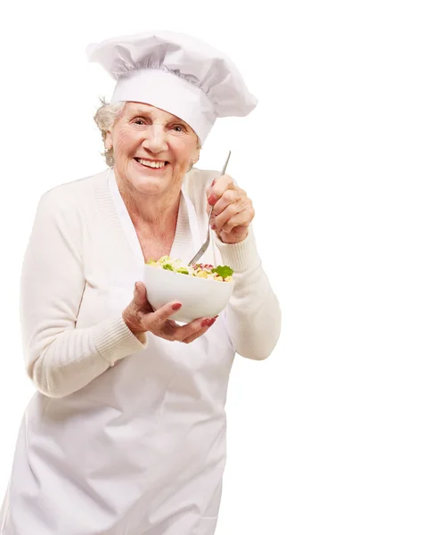 Portrait d'adorable cuisinière senior mangeant de la salade contre un wh — Photo
