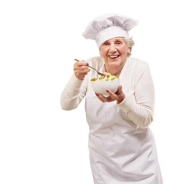 Retrato de cocinera senior comiendo ensalada sobre blanco — Foto de Stock