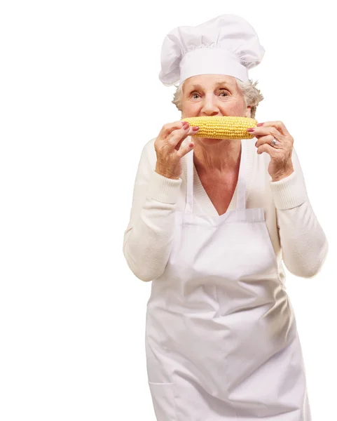Портрет старшої кулінарної жінки, що їсть кукурудзяний коб на білому фоні — стокове фото