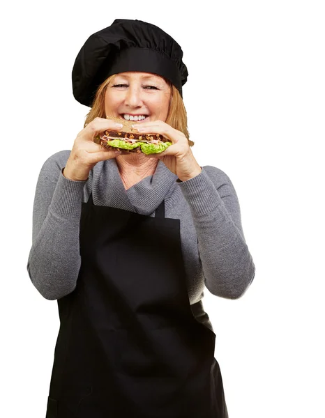 Mulher cozinheira de meia idade segurando um sanduíche vegetal sobre o bac branco — Fotografia de Stock