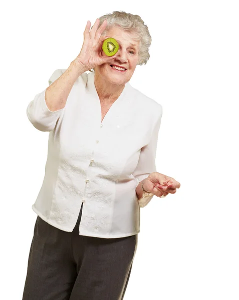 Portrait of senior woman holding kiwi in front of her eye over w — Stock Photo, Image
