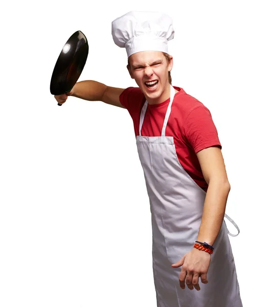 Портрет разгневанного молодого повара, бьющего сковородкой по белому берегу — стоковое фото