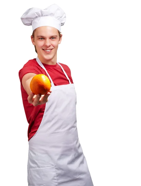 Portrait of young cook man offering orange over white background — Stock Photo, Image