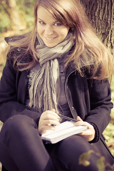 Una ragazza scrive su un blocco nel parco — Foto Stock