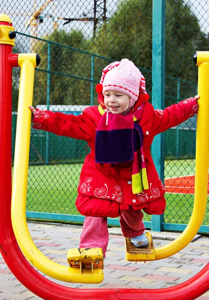 Das kleine Mädchen in Winterbekleidung beschäftigt sich mit Fitnessgeräten im Freien — Stockfoto
