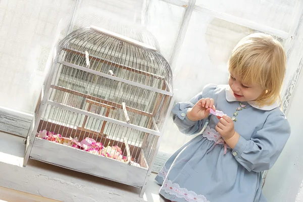 Das kleine Mädchen in einem Kleid sitzt neben einem Fenster mit einer Zelle — Stockfoto