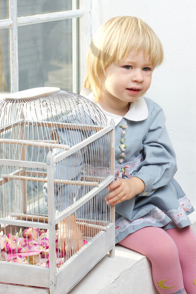 Маленькая девочка в платье сидит у окна с камерой
