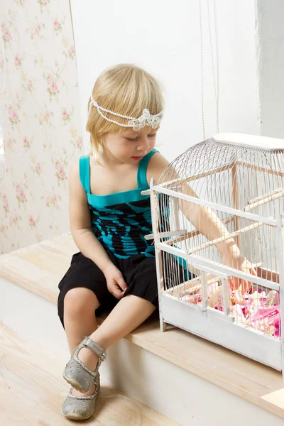 La bambina in un vestito seduta vicino a una finestra con una cella — Foto Stock