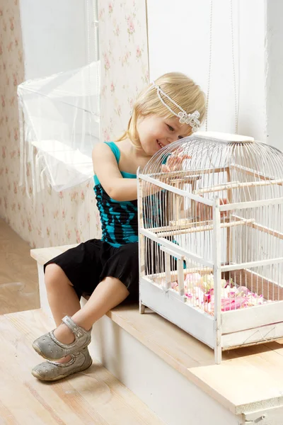 Den lilla flickan i en klänning som sitter nära ett fönster med en cell — Stockfoto