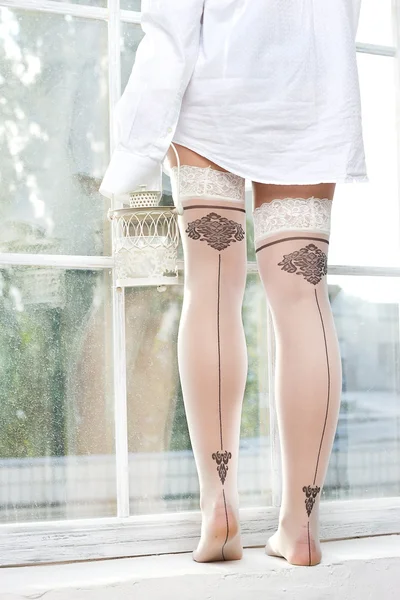 Vrouwelijke benen in kousen in de buurt van het venster — Stockfoto