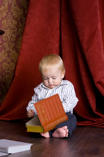 Junge liest ein Buch auf dem Boden sitzend gegen — Stockfoto