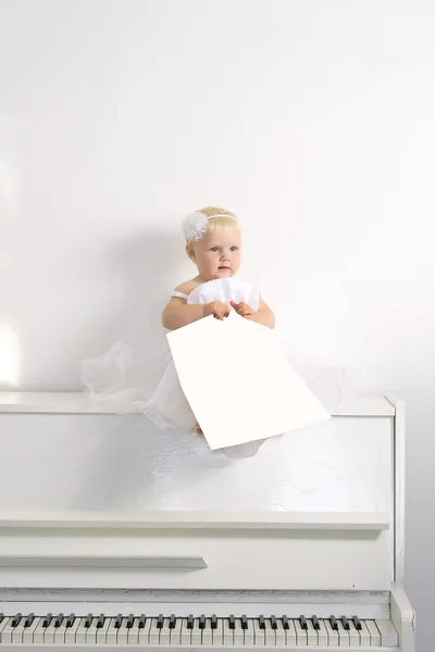 Una chica vestida de blanco sentada en un piano en la habitación — Foto de Stock