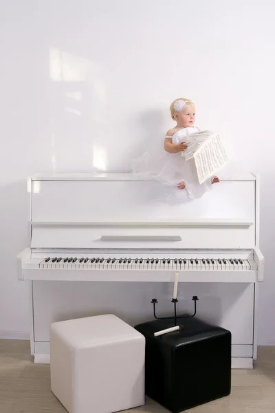 坐在房间里的钢琴上的白色连衣裙的女孩 — 图库照片