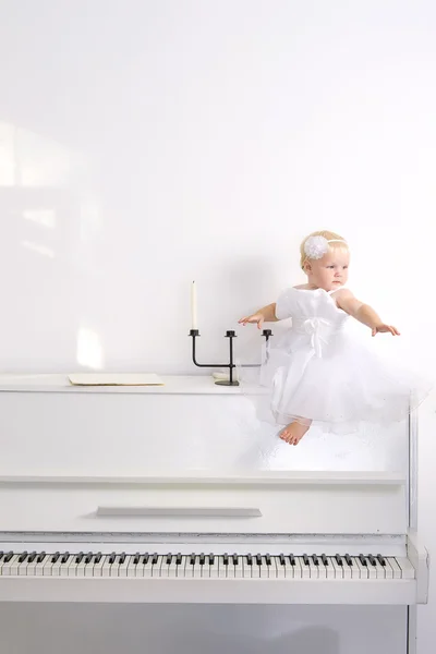 坐在房间里的钢琴上的白色连衣裙的女孩 — 图库照片