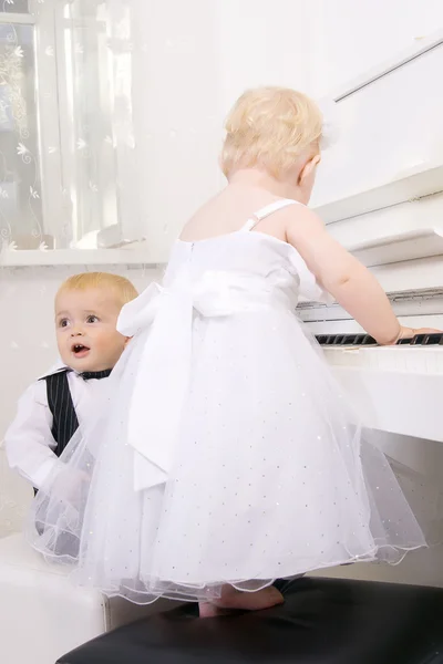 Jongen en meisje op een witte piano spelen — Stockfoto