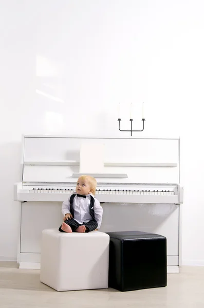 Boy in a suit sitting reins white piano — Stock Photo, Image