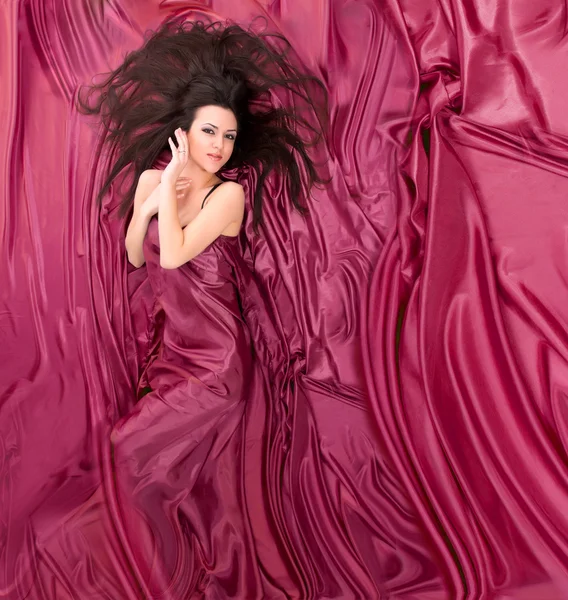 Dívka s dlouhými tmavými vlasy, ležící na pozadí fialové s — Stock fotografie