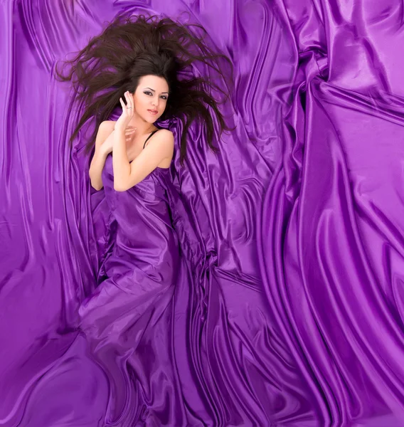 Menina com longos cabelos escuros deitado contra um fundo de roxo s — Fotografia de Stock