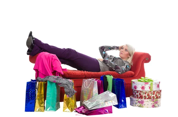 Втомилася жінка лежить на червоному дивані, навколо сумки для покупок в па — стокове фото