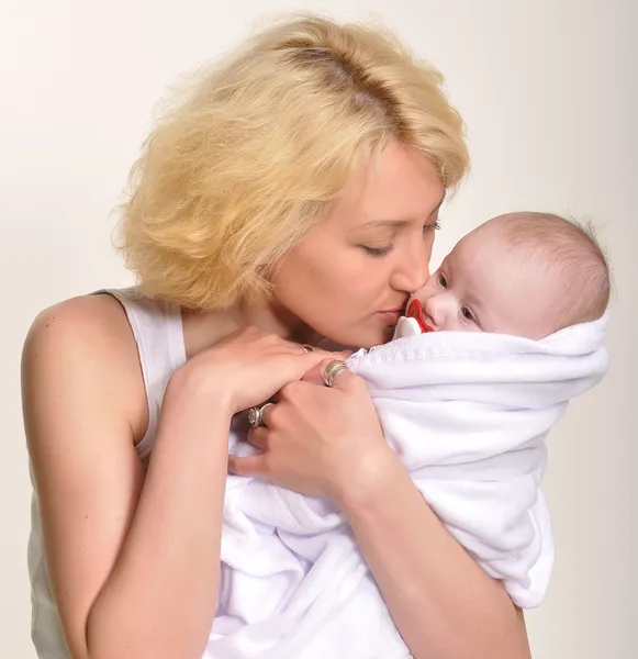 Una joven madre rubia sostiene a su bebé amortiguado en sus brazos y lo besa — Foto de Stock