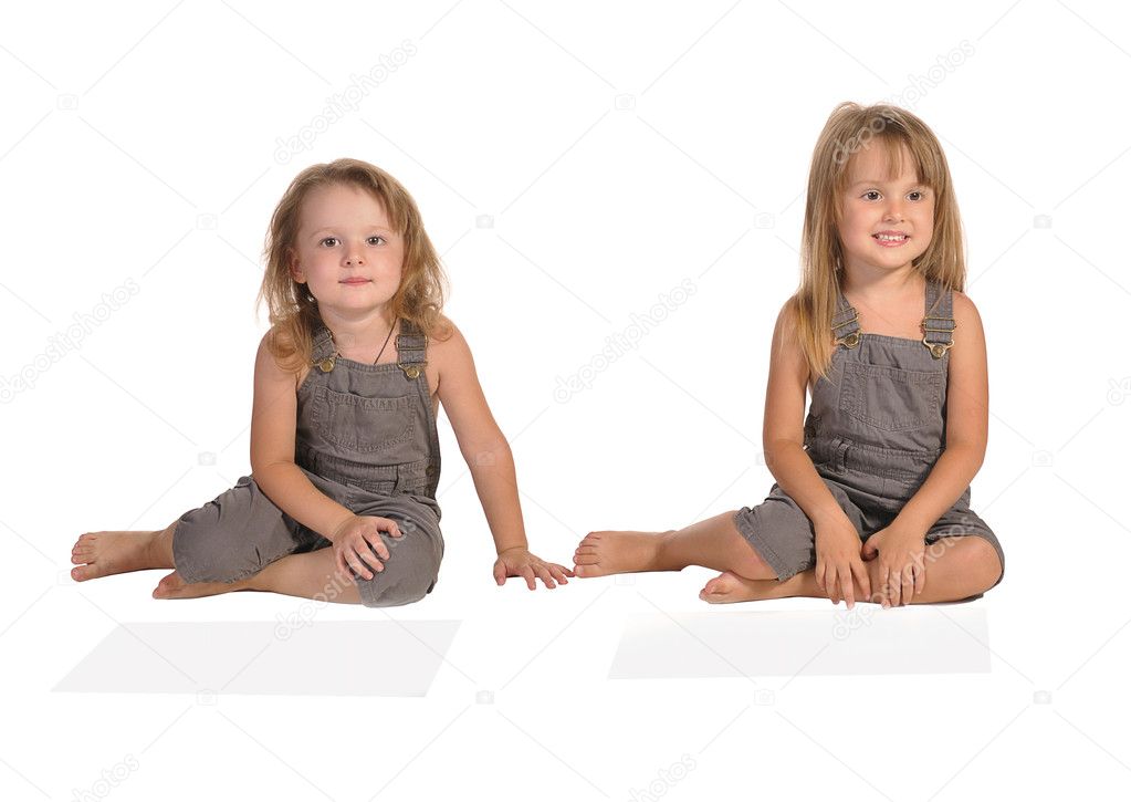 Twins sisters in rompers sitting isolated on white background