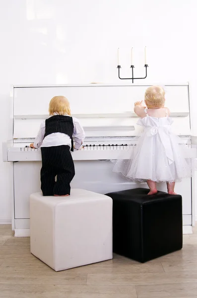 Menino e menina tocando em um piano branco — Fotografia de Stock