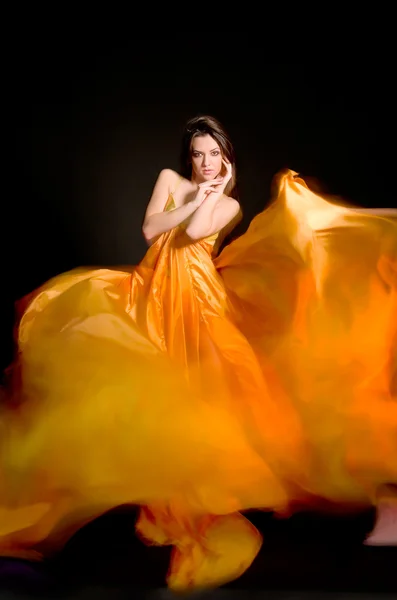 Όμορφο κορίτσι στο πορτοκαλί φόρεμα από το πέταγμα ύφασμα — Φωτογραφία Αρχείου