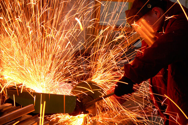 Worker white hot sparks at grinding steel material