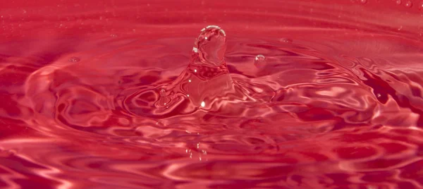Rozpryskiwania kropelki wody na czerwonym tle — Zdjęcie stockowe
