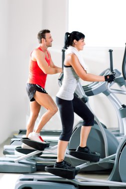 Man and woman with elliptical cross trainer at gym clipart