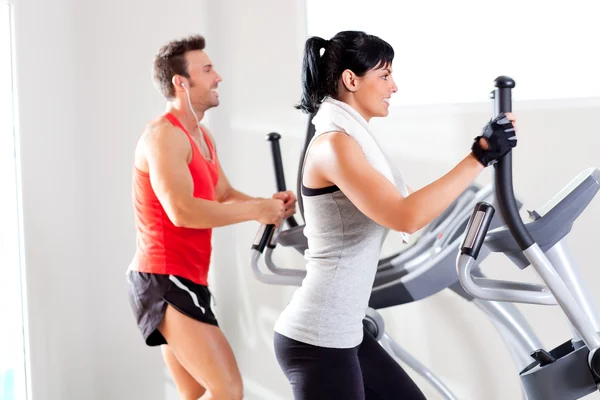 Mann und Frau mit Crosstrainer im Fitnessstudio — Stockfoto