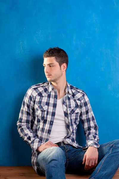 Bonito jovem com camisa xadrez sentado em madeira — Fotografia de Stock