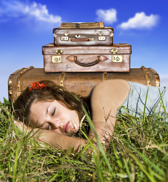 Traveling young woman resting in a field with her suitcases