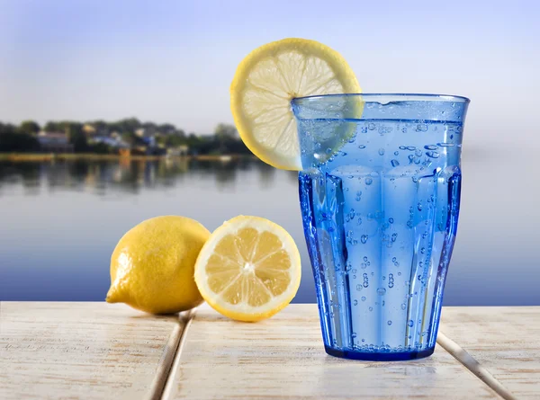 Голубой стакан с газированной водой и лимоном на деревянной палубе с видом на спокойную воду тропической лагуны — стоковое фото